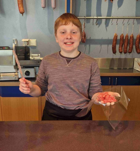 Junge mit Gehacktem hinter einer Fleischtheke