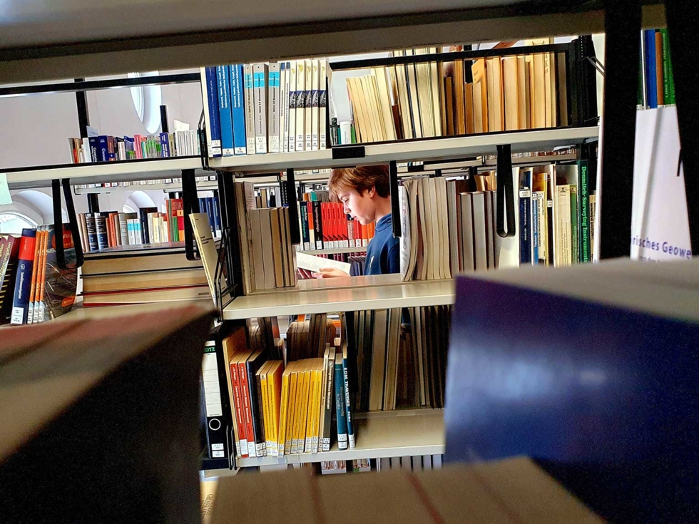 Boys'Day-Teilnehmer hinter einem Bücherregal liest ein Buch