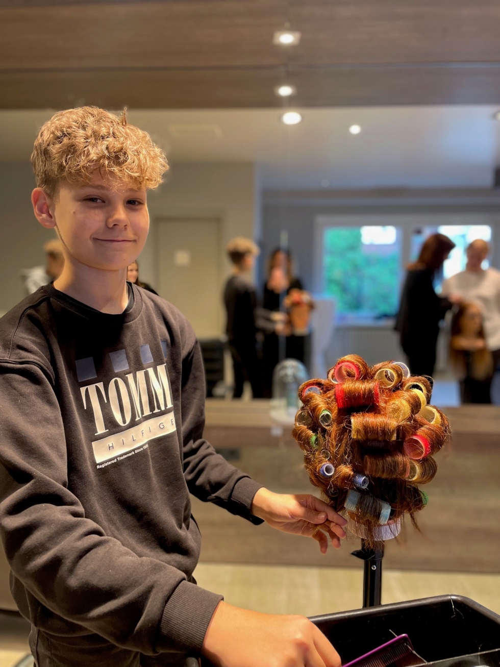 Boys'Day-Teilnehmer wickelt Locken an einen Frisierkopf