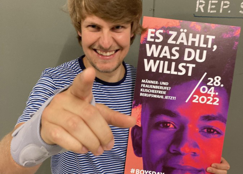 Junger Mann zeigt in die Kamera und hält Plakat vom Boys'Day