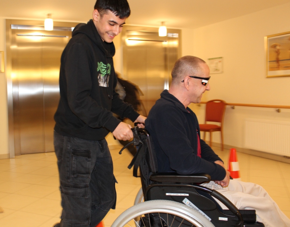 Boys'Day-Teilnehmer schiebt Mann im Rollstuhl