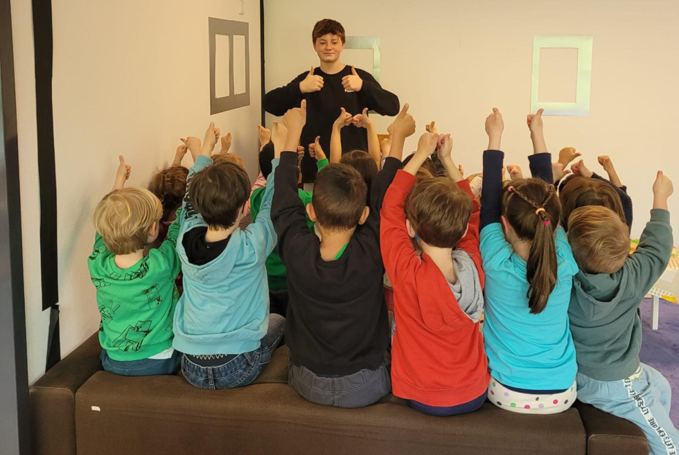 Junge mit Daumen hoch vor Kindergartenkindern